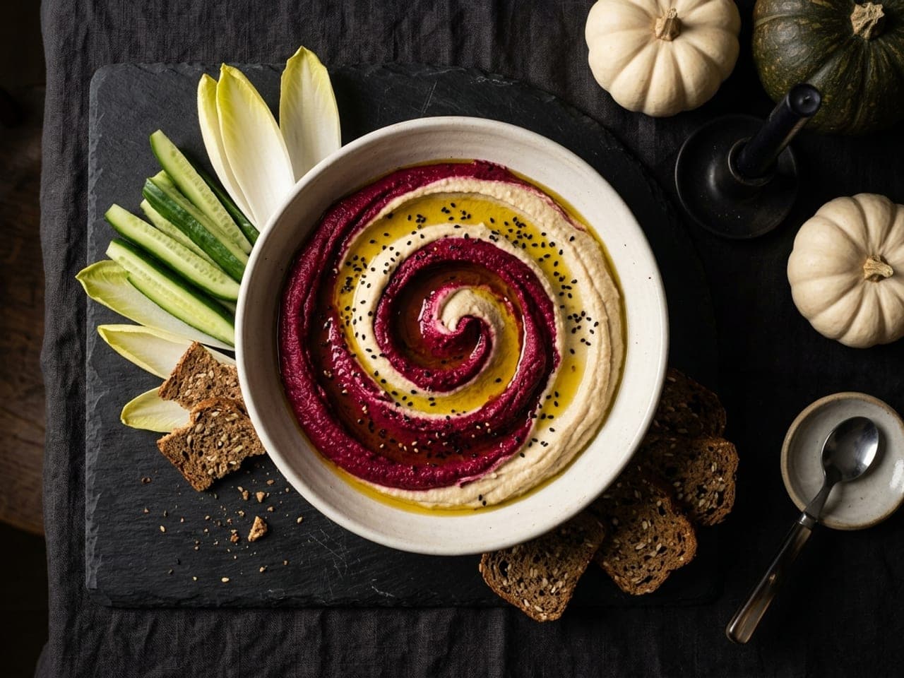 A shallow pale bowl of hummus swirled deep magenta and cream in a spiral, olive oil in the grooves and black sesame seeds scattered on top