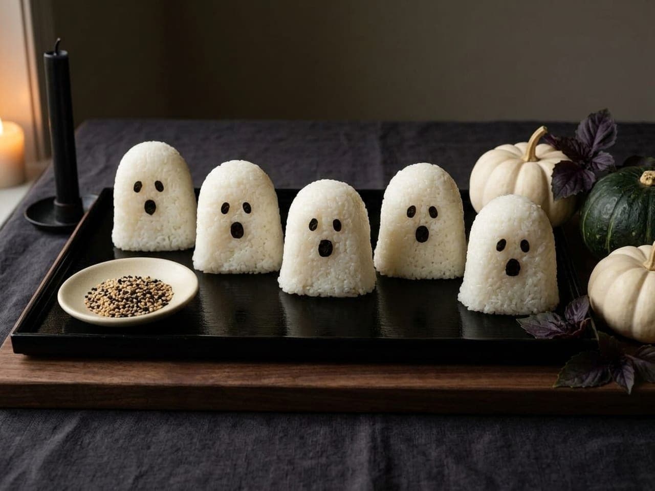 White rice balls shaped like little ghosts with nori eyes and mouths, lined up on a dark lacquer tray