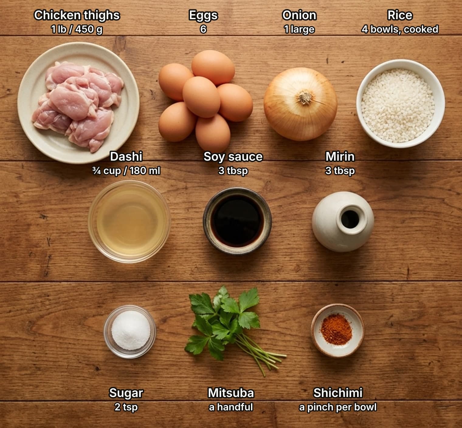 All ten oyakodon ingredients laid out overhead on a wooden kitchen counter and labelled with quantities: chicken thighs, six eggs, an onion and short-grain rice on top; dashi, soy sauce and mirin in the middle; sugar, mitsuba and shichimi below.