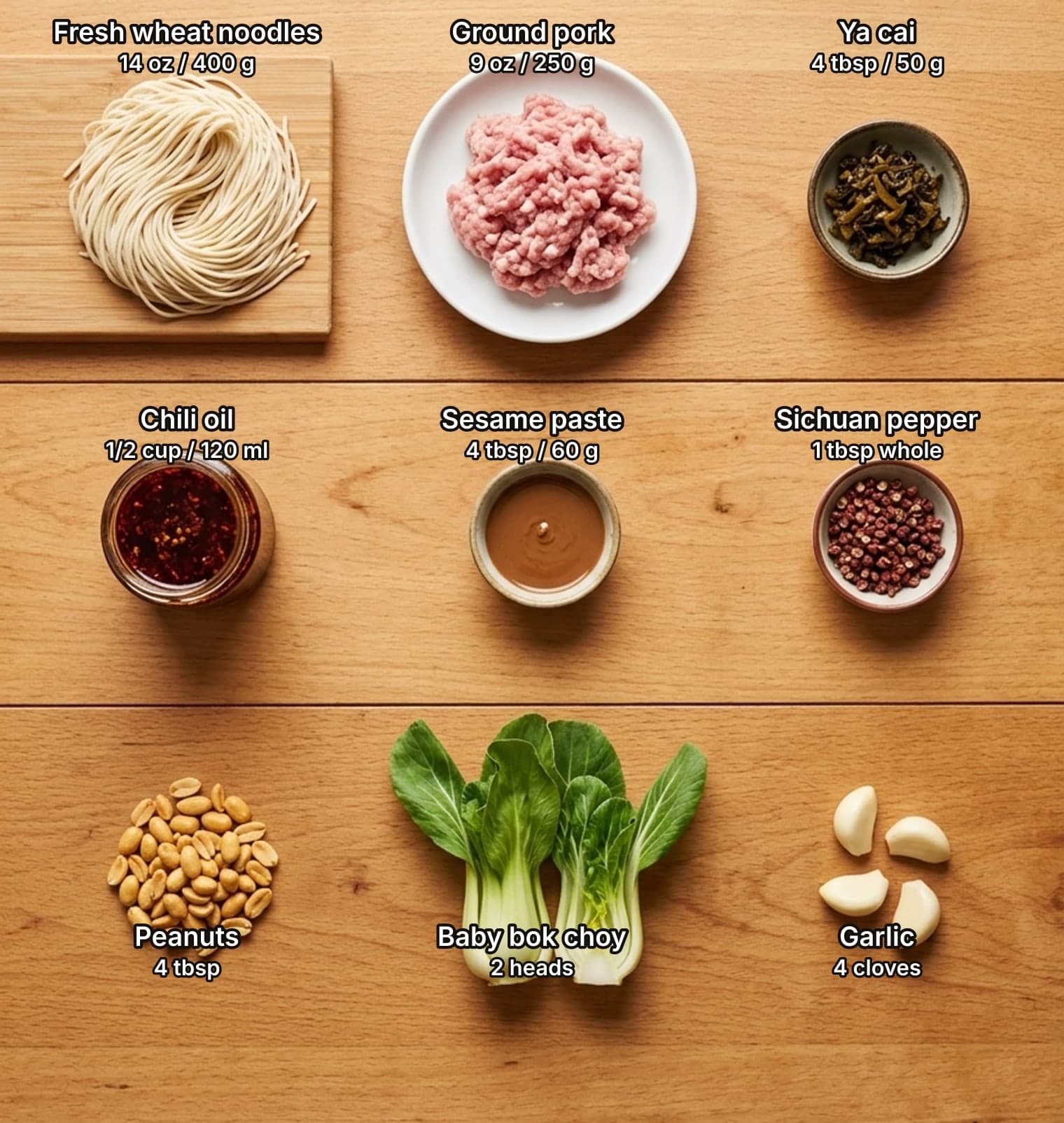 Ingredients for dan dan noodles laid out overhead on a wooden kitchen counter and labelled with quantities: a nest of fresh thin wheat noodles, raw ground pork and a small bowl of dark preserved mustard greens on top; a jar of red chili oil, a bowl of brown sesame paste and whole Sichuan peppercorns in the middle; roasted peanuts, baby bok choy and garlic cloves below.