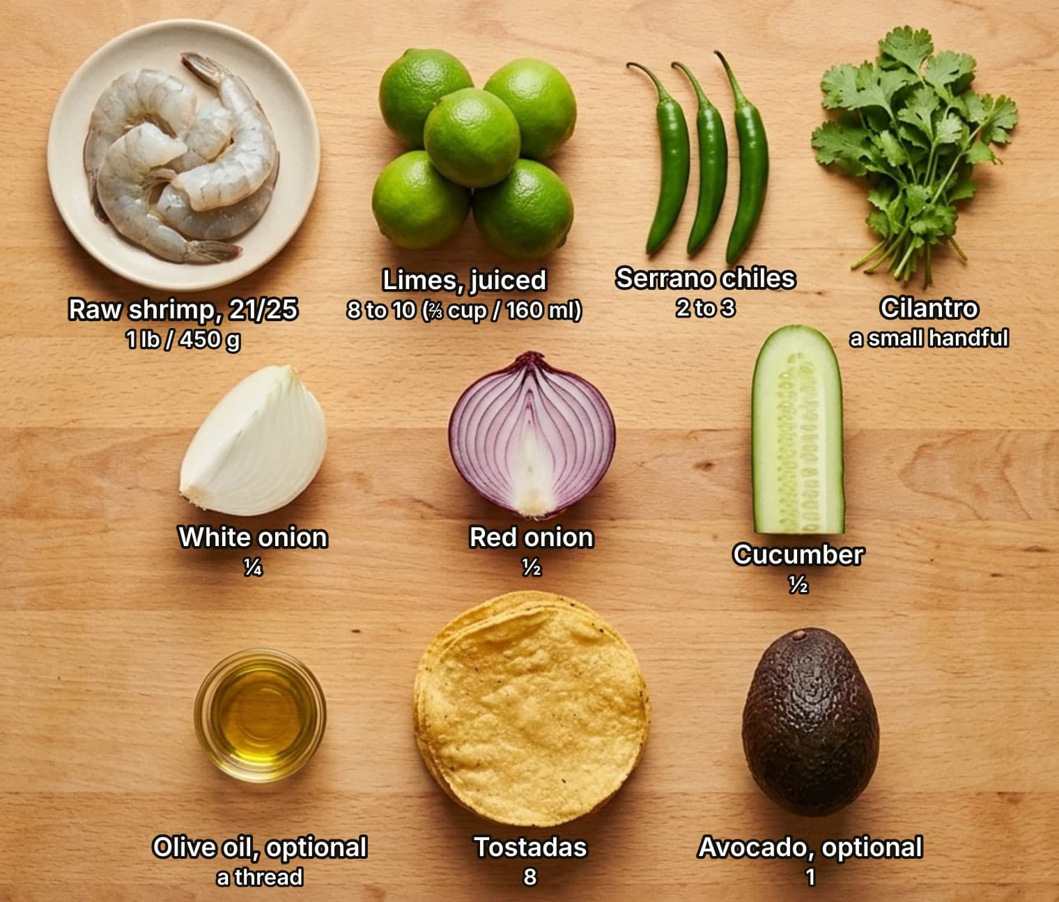 Aguachile ingredients laid out overhead on a wooden counter and labelled with quantities: large raw shrimp on a plate, a pile of limes, three serrano chiles and a bunch of cilantro across the top; a wedge of white onion, half a red onion and half a cucumber in the middle; a small glass dish of olive oil, a stack of tostadas and an avocado below.