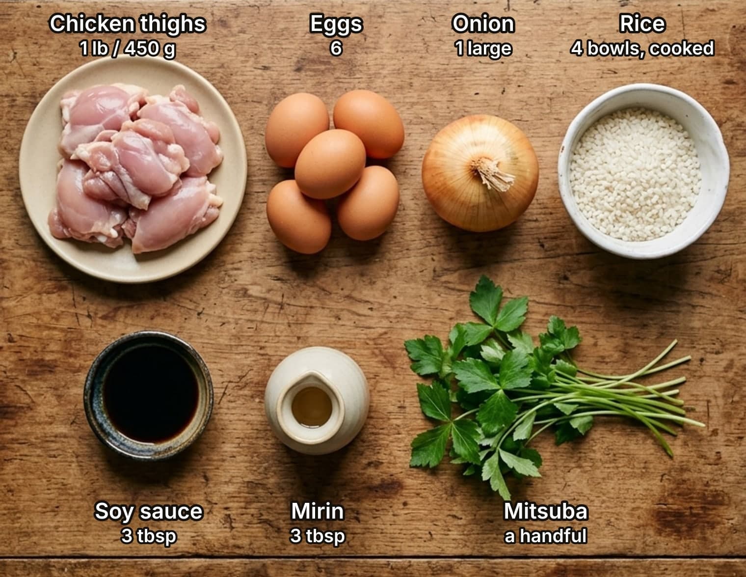 Ingredients for oyakodon laid out overhead on a wooden kitchen counter and labelled with quantities: chicken thighs on a plate, six eggs, an onion and a bowl of short-grain rice, with a dish of soy sauce, a small flask of mirin and a bunch of mitsuba below.