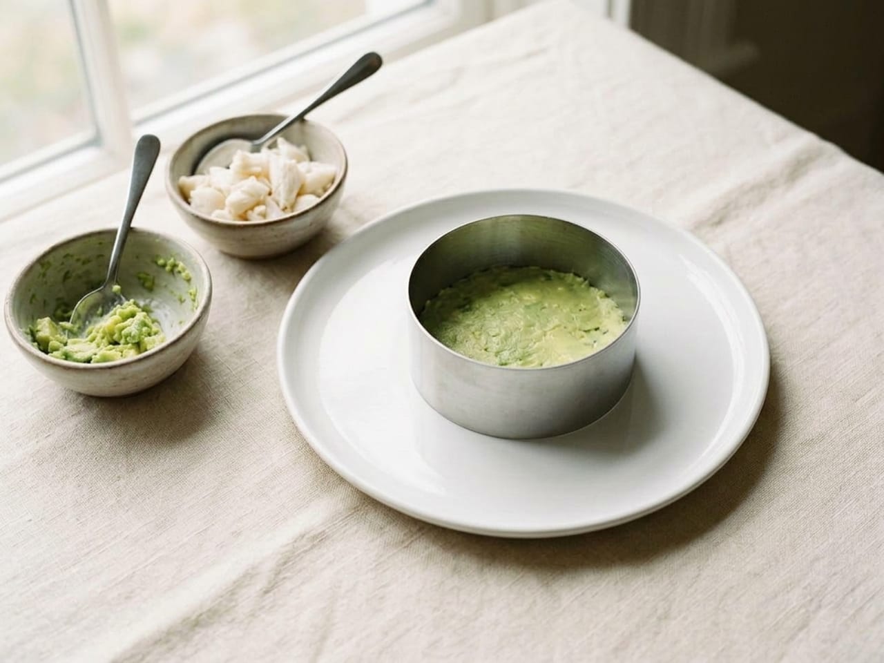 The same ring mold on the same white plate, with a flat, pressed layer of mashed avocado now filling its bottom